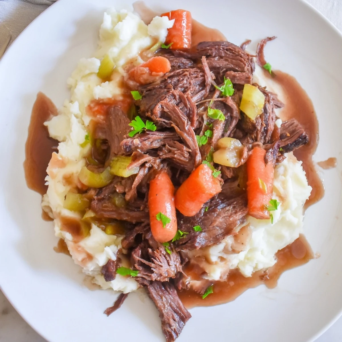 Savory slow cooker pot roast resting alongside rich, fluffy mashed potatoes drizzled with gravy.