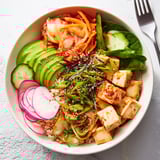 Deliciously vibrant fermented vegetable bowl topped with sliced avocado and tangy dressing.  