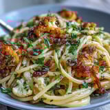 Fresh lemon zest and parsley garnish this Italian-inspired Cauliflower, Anchovy and Raisin Spaghetti, served on a rustic plate.