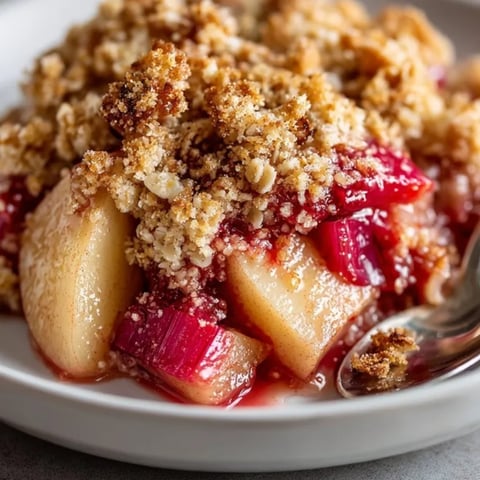 Golden brown apple rhubarb crisp with bubbly fruit filling, served warm in a rustic baking dish.