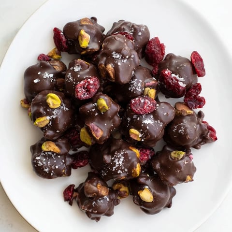 Pistachio and dried cranberry clusters: a close-up shows crunchy nuts and ruby cranberries in melted dark chocolate.