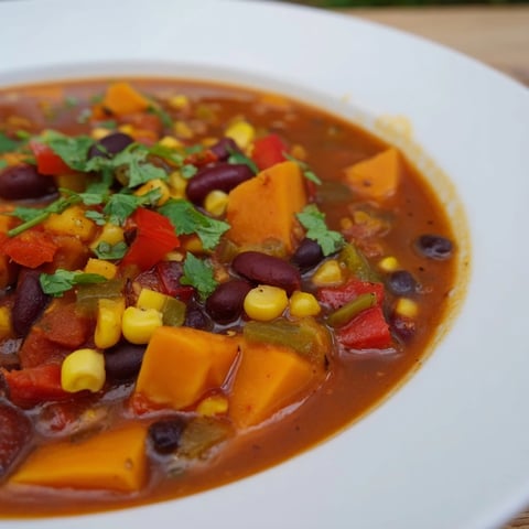 Steaming bowl of Smoky Sweet Potato Chili with rich, red hues served in a rustic ceramic dish.