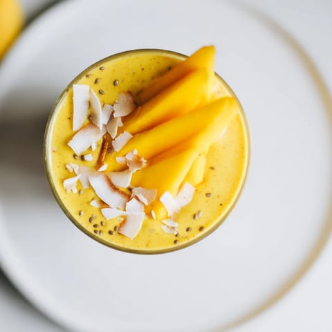 Creamy mango turmeric smoothie, a bright yellow blend garnished with fresh mango slices.