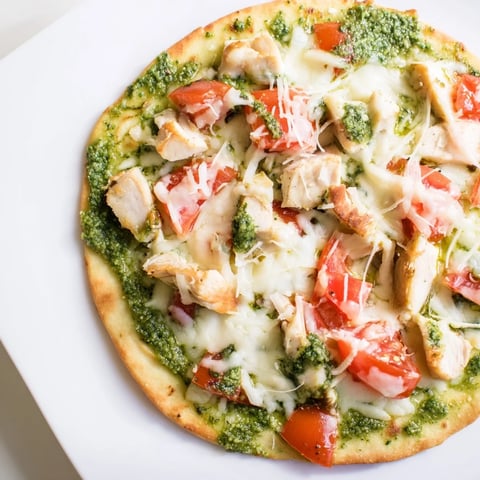 Golden, bubbly mozzarella covers a thin-crust Chicken Pesto Pizza with tomato slices and fresh basil.
