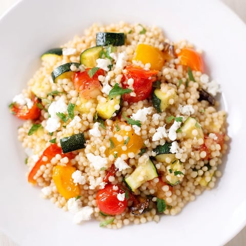A bowl of Roasted Veggie Couscous Salad with colorful roasted zucchini, bell peppers, and cherry tomatoes tossed in a bright lemon dressing, topped with feta and toasted pine nuts.