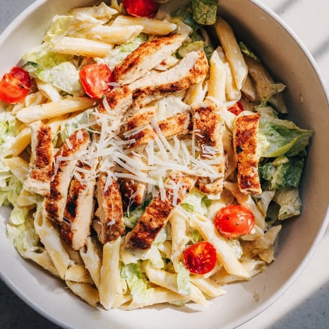 A close-up of a bowl of Spicy Chicken Caesar Pasta, showcasing grilled chicken slices, creamy dressing, and crisp romaine on penne noodles.