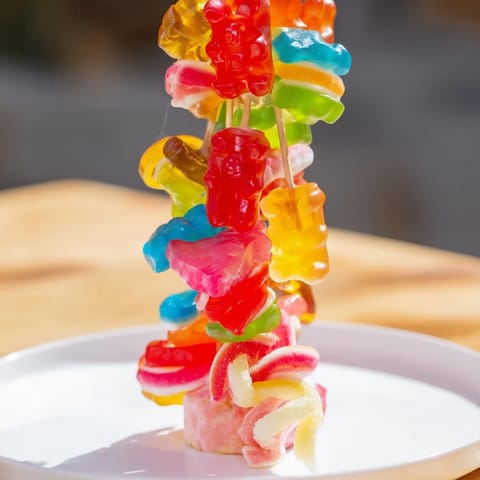Sweet and colorful gummy candy kabobs, ready to eat, featuring gummy bears and worms on skewers.