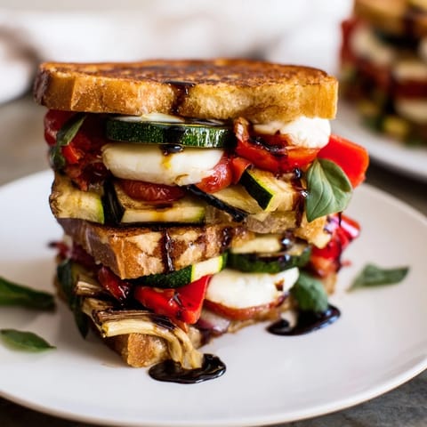 Melted mozzarella oozes from a sheet-pan roasted veggie caprese grilled cheese, served with fresh basil.