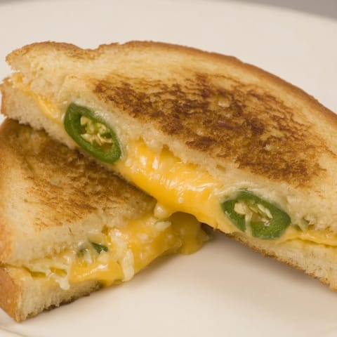 Two golden, buttery Jalapeño Popper Grilled Cheese sandwiches sit on a white ceramic plate.