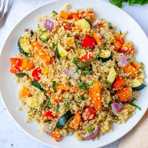 Colorful roasted vegetable quinoa pilaf served warm as a vibrant main dish, with lemon juice and fresh herbs for brightness.