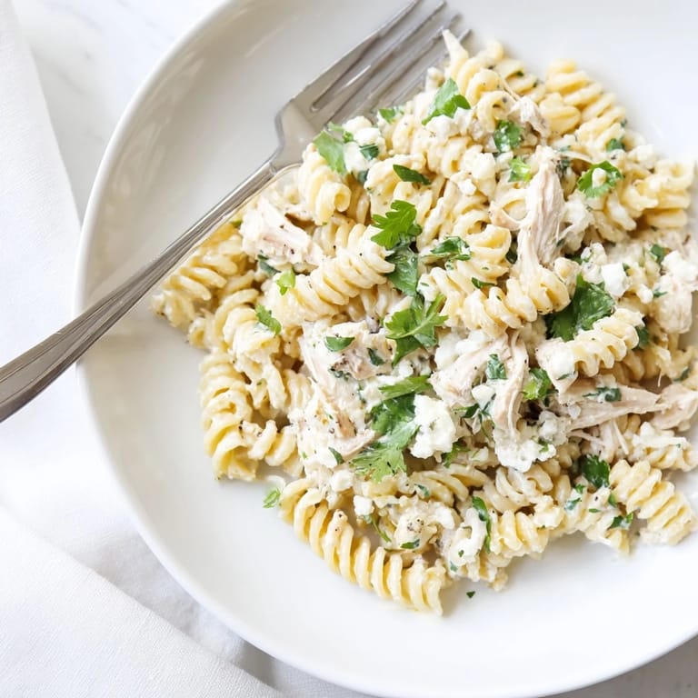 Shredded chicken and rotini pasta tossed in tangy cilantro lime yogurt sauce, served warm in a white bowl.