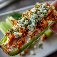Keto buffalo chicken stuffed celery boats with blue cheese crumble on a white platter.