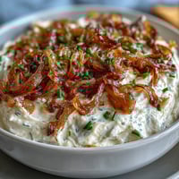 Creamy caramelized onion dip with Greek yogurt base, served with crispy potato chips and fresh vegetable sticks.