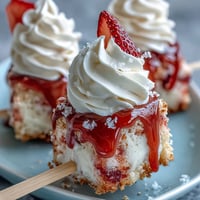 Delectable mini strawberry shortcake bites on skewers, topped with fluffy whipped cream.